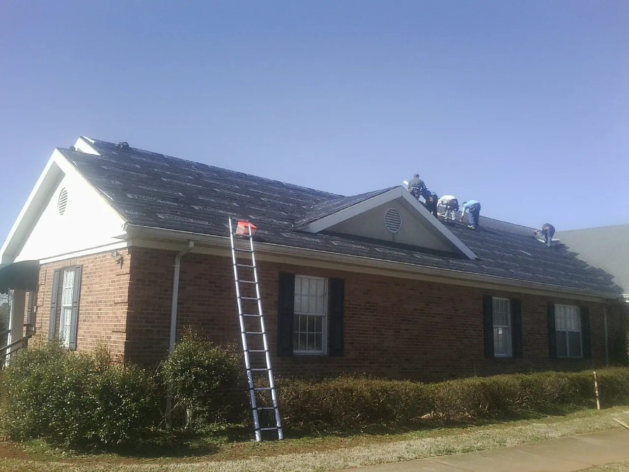 Crew tearing shingles off a brick ranch roof with a ladder set — Metal Roof Repair work by our crew in Mitchell