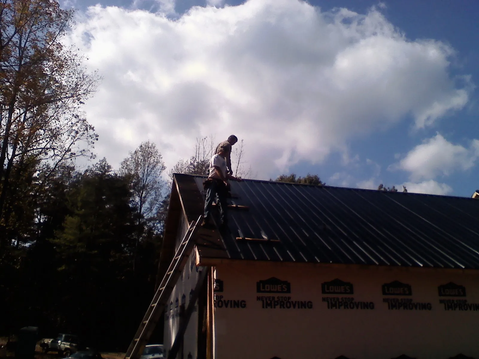 Roofer fastening dark metal panels high against a cloudy sky, from a Roof Inspection job in Mitchell