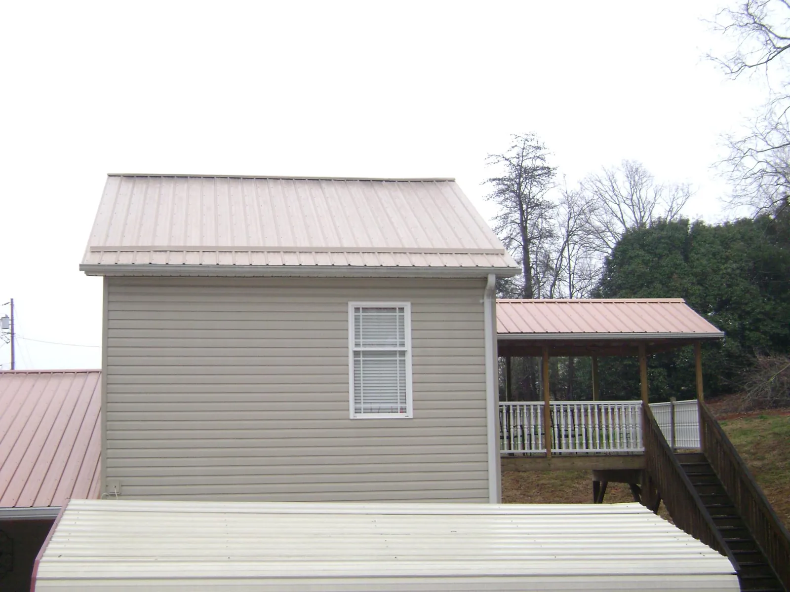 Tan metal roofs on a two story addition and attached porch, from a Roof Replacement job in Mitchell
